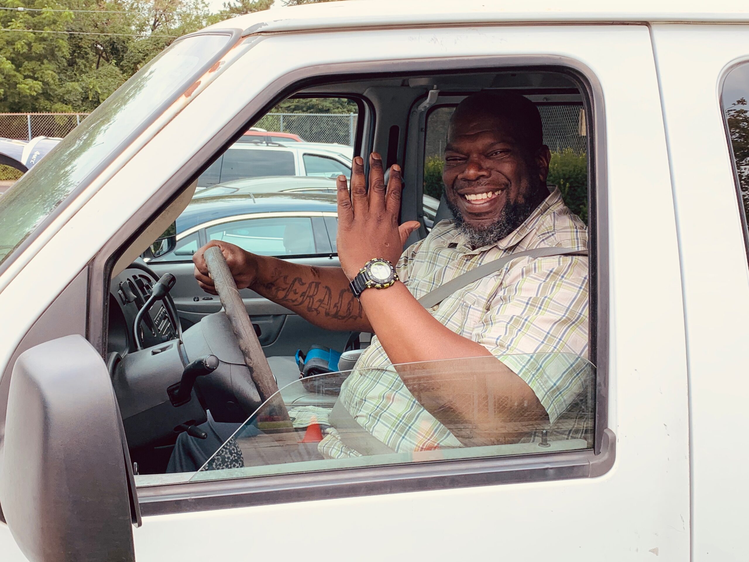 Hope Hall employee, an African American man waving and smiling from the driver's seat of a van.