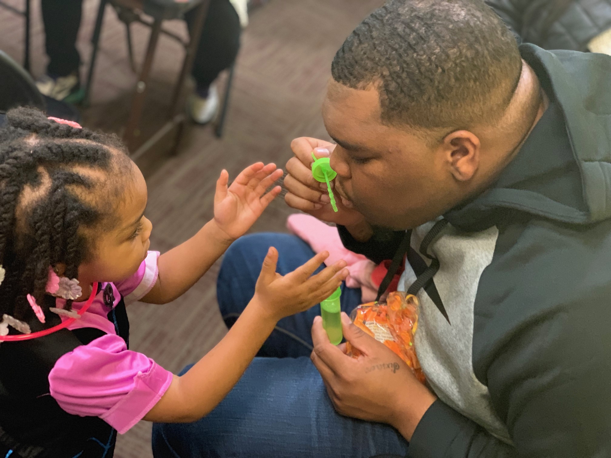 An African American man blowing bubbles with a young girl. 