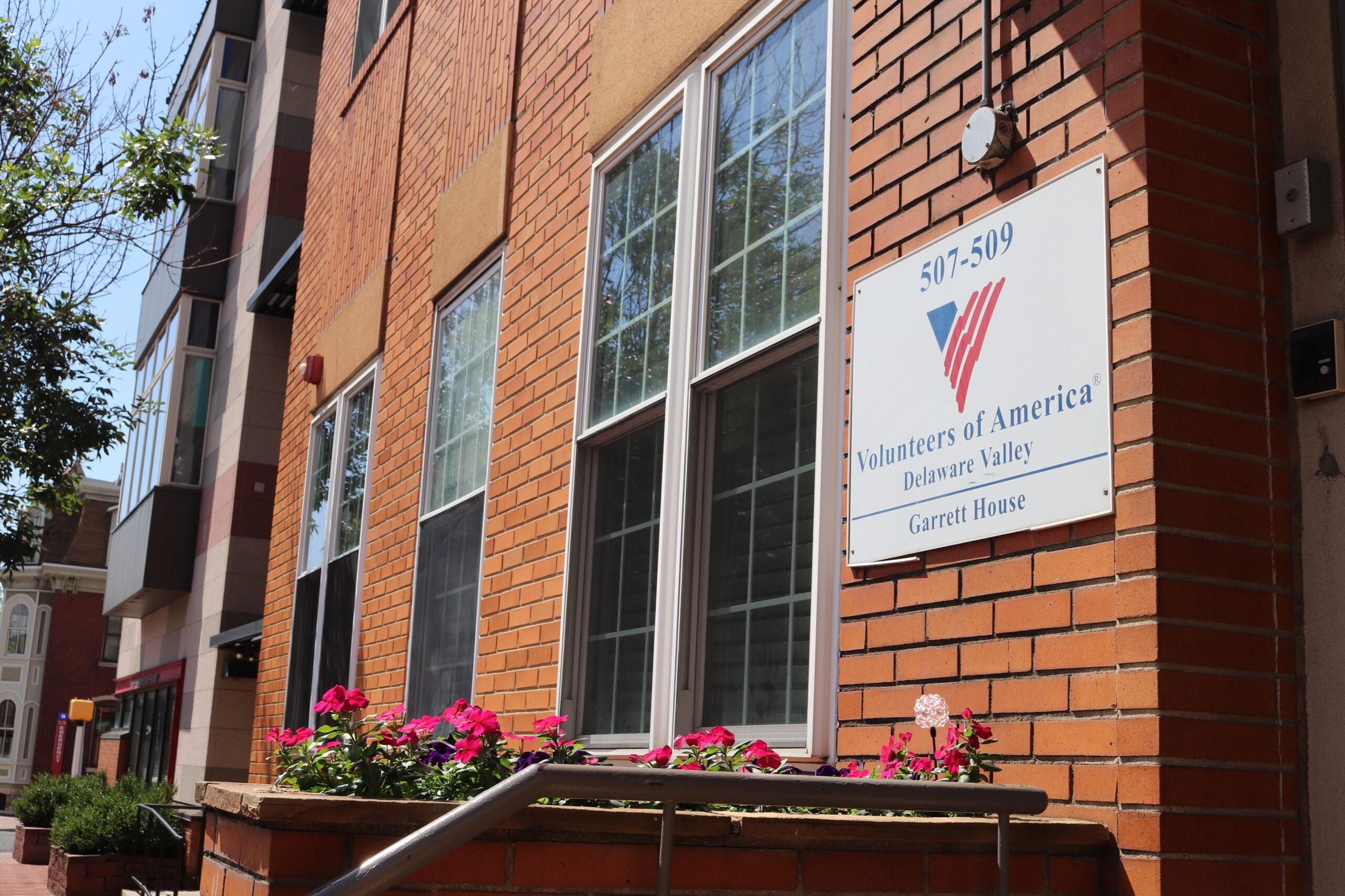 A close up of the Garrett House sign with pink flowers in the foreground and the building in the background.