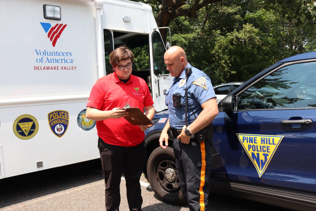 A VOADV staff member and a police officer look at a clipboard in front of an IMPACT mobile unit and a police car.